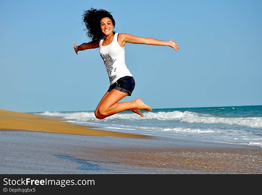 Woman in White Tanktop Jump over Beach Sand