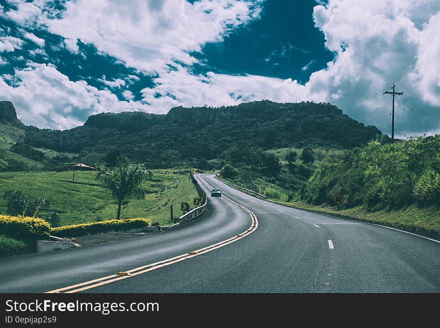 Car driving on winding country road through green fields against blue skies. Car driving on winding country road through green fields against blue skies.