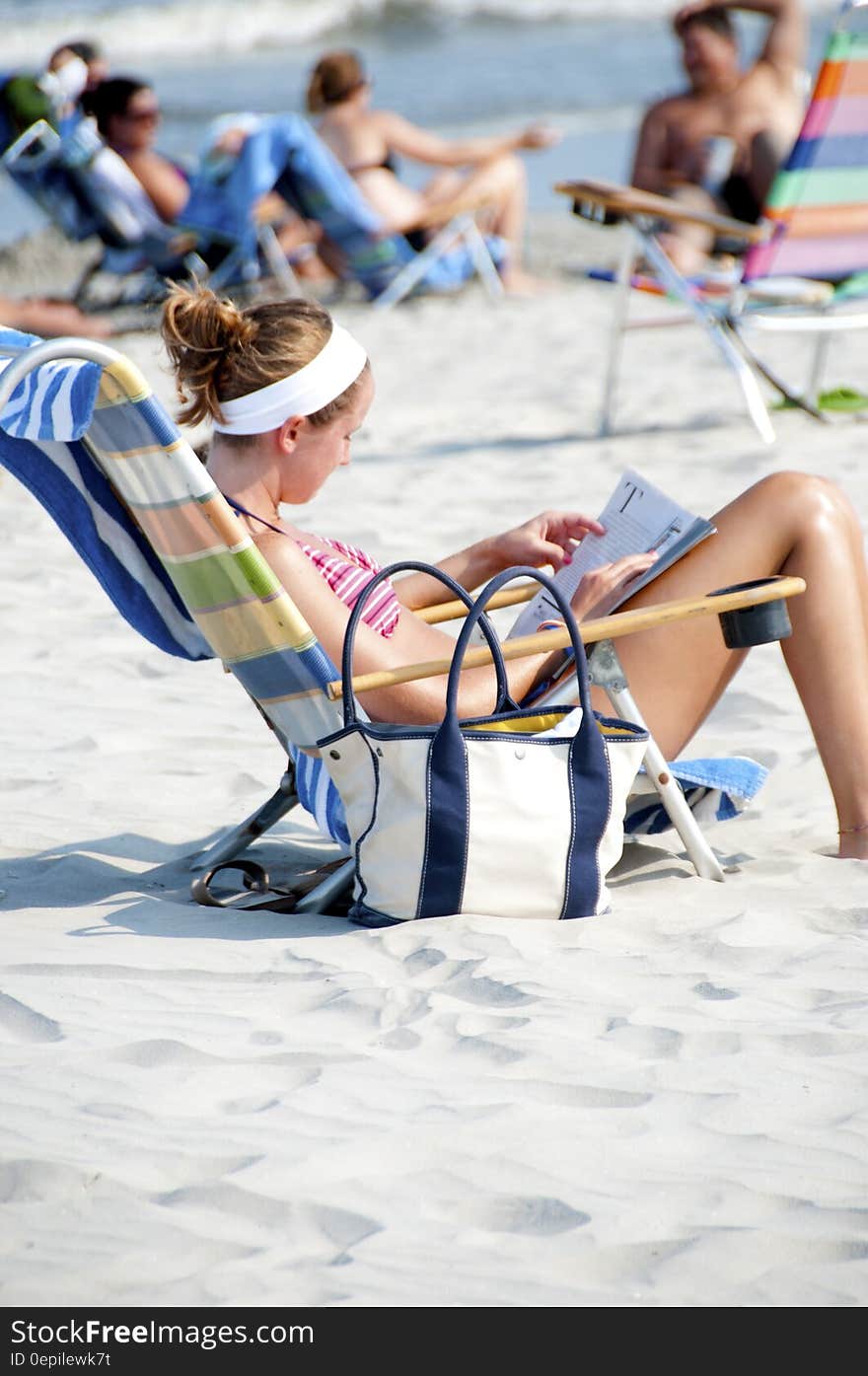 Woman Sitting on the Lounge Chair Reading Magazine on the Beach during Nighttime