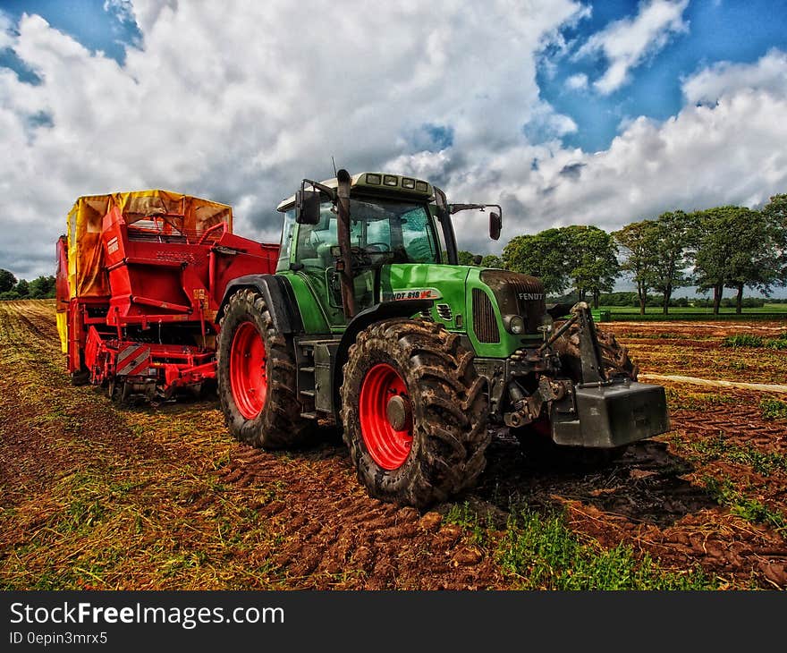 Green Tractor Pulling Red Bin on Field at Daytime