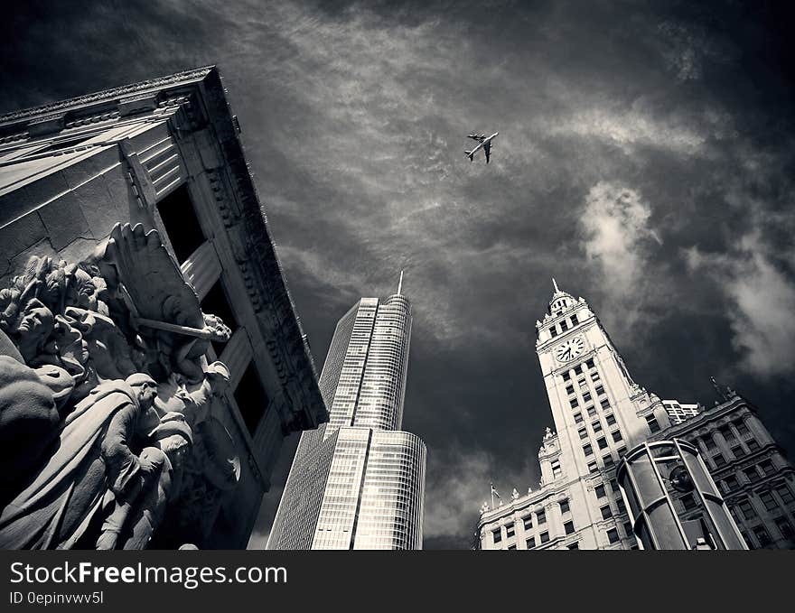 Air Plane Flying over Concrete Buildings and Statues in Grayscale Photography