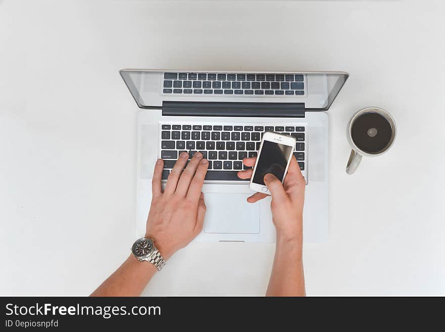 Overhead of hands typing on laptop computer and smartphone touchscreen with mug of coffee. Overhead of hands typing on laptop computer and smartphone touchscreen with mug of coffee.