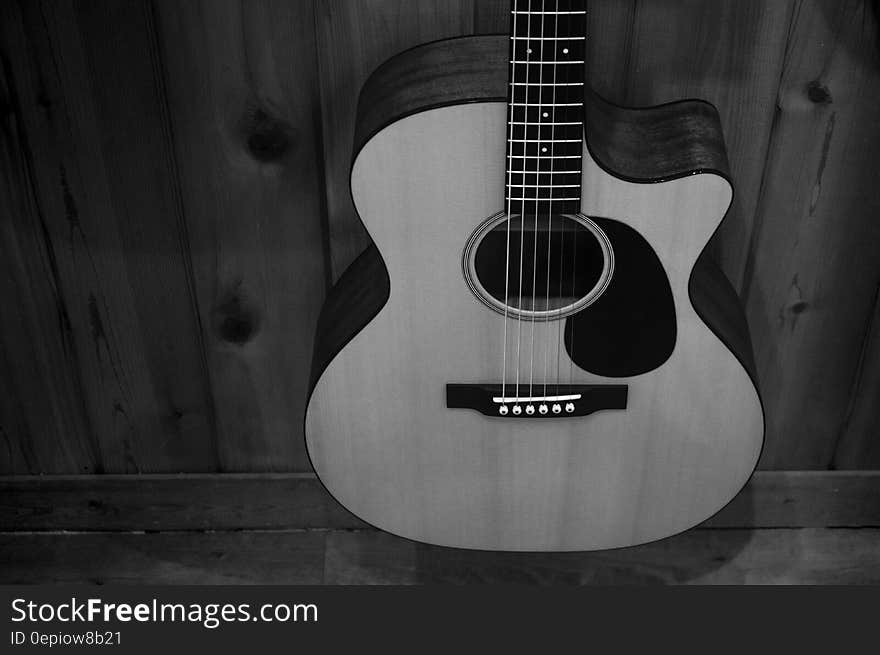 Greyscale Photo of Acoustic Guitar on Wooden Fence