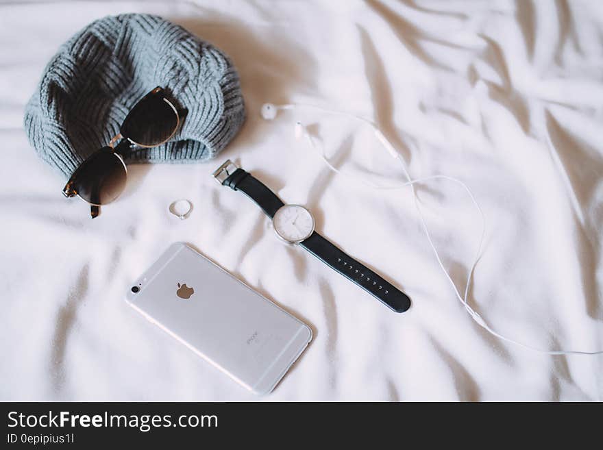 Watch, iphone, sunglasses, ring and small gray textured bag (or hat) laid on a white duvet or bedspread. Watch, iphone, sunglasses, ring and small gray textured bag (or hat) laid on a white duvet or bedspread.