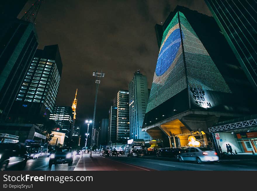 Cars Traveling on Road Between Buildings during Nighttime