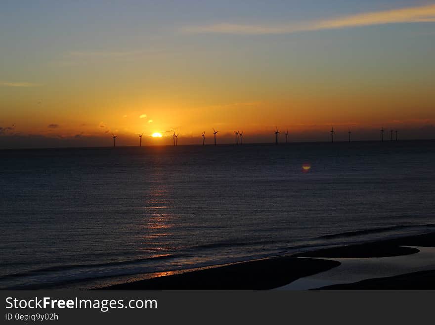 Silhouette of offshore windmills in water at sunset. Silhouette of offshore windmills in water at sunset.