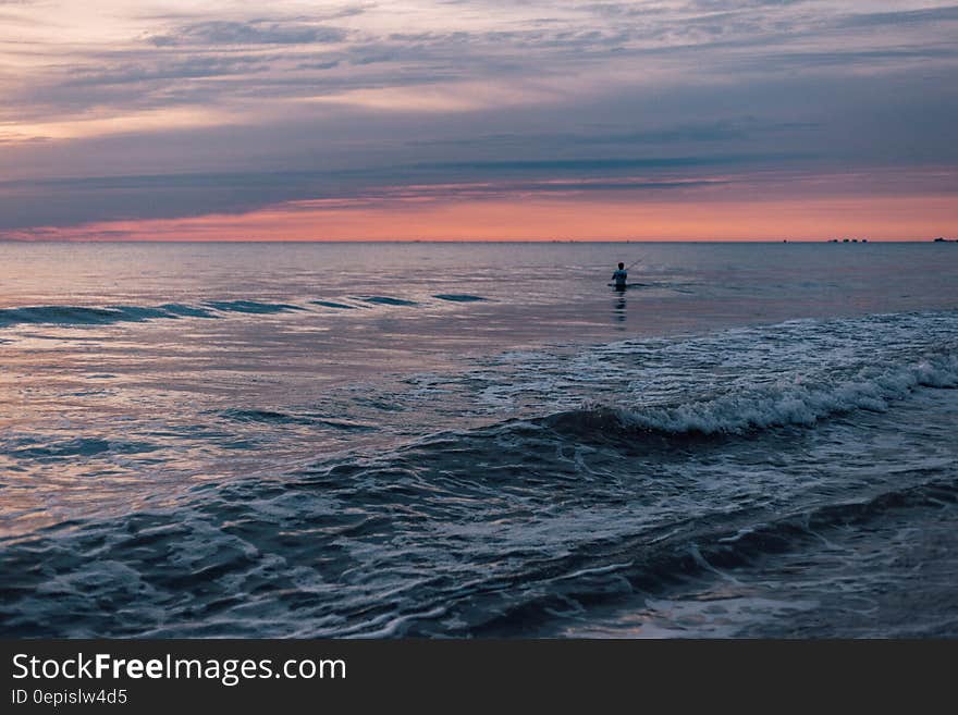 Person Standing in the Sea during Sunset