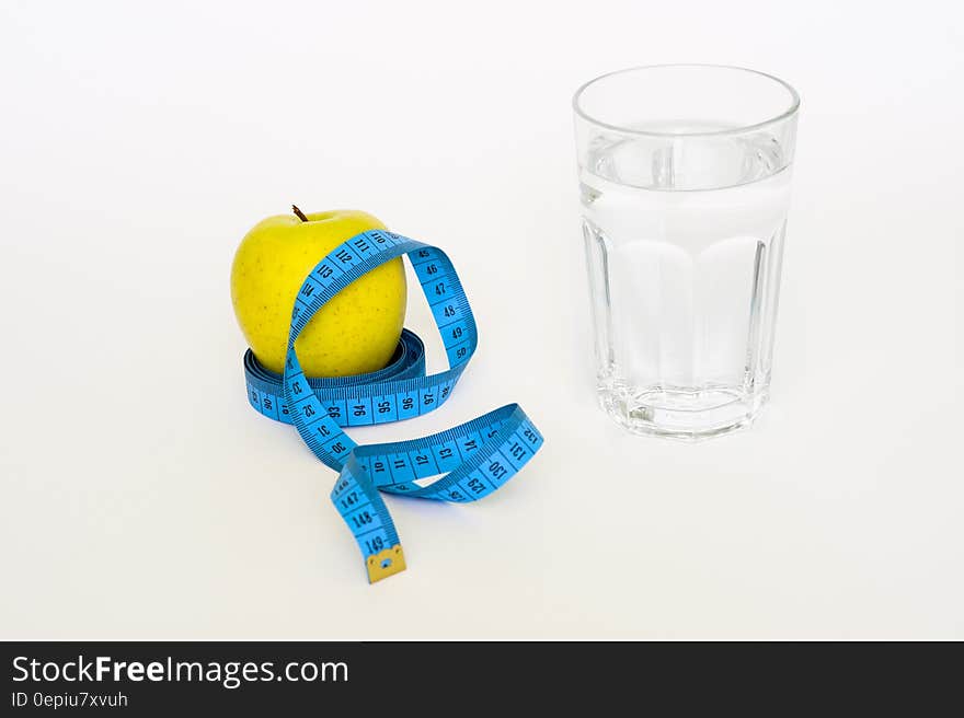 Clear Drinking Glass Near in Blue Tape Measure and Apple Fruit