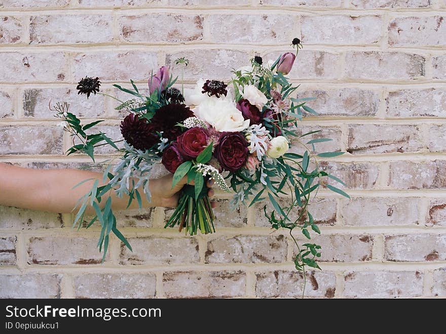 Hand holding bouquet of flowers outdoors against brick wall on sunny day. Hand holding bouquet of flowers outdoors against brick wall on sunny day.