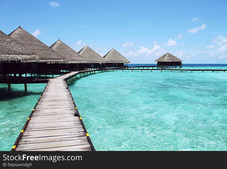 Empty wooden boardwalk between grass thatched bungalows over blue waters in Tahiti. Empty wooden boardwalk between grass thatched bungalows over blue waters in Tahiti.