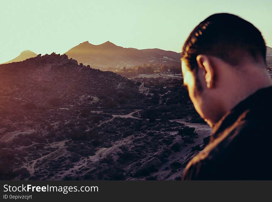 Back of man overlooking mountain valley on sunny day.