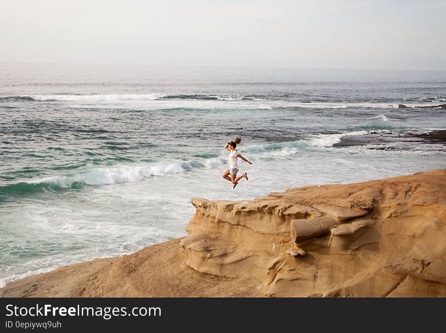 Women Wearing White Shirt Jumping on Shore