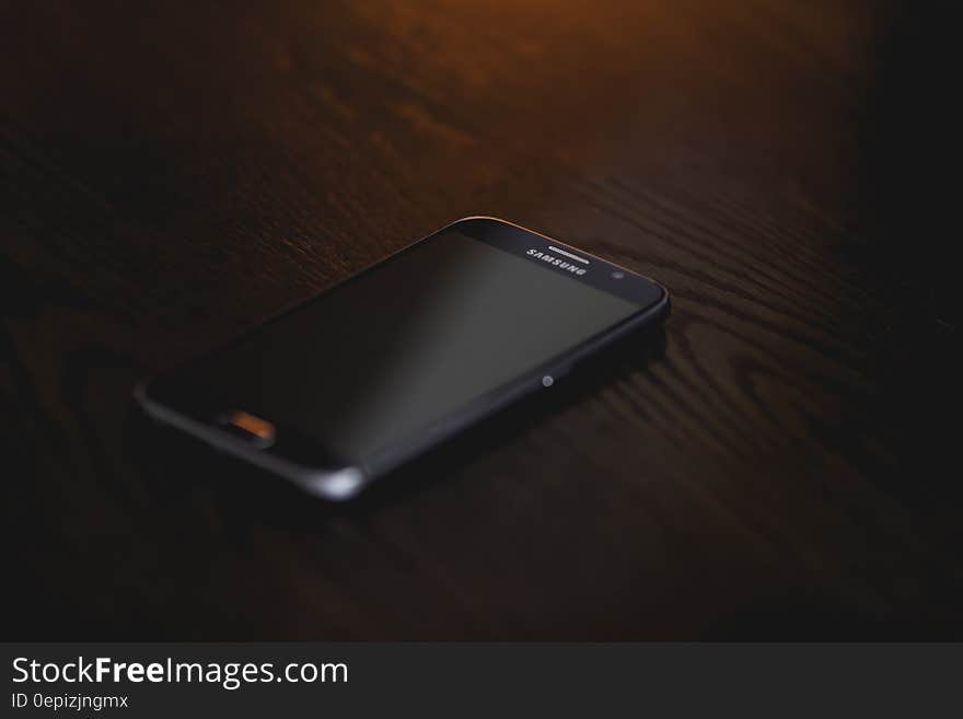 Black Samsung Smartphone at Brown Wooden Surface