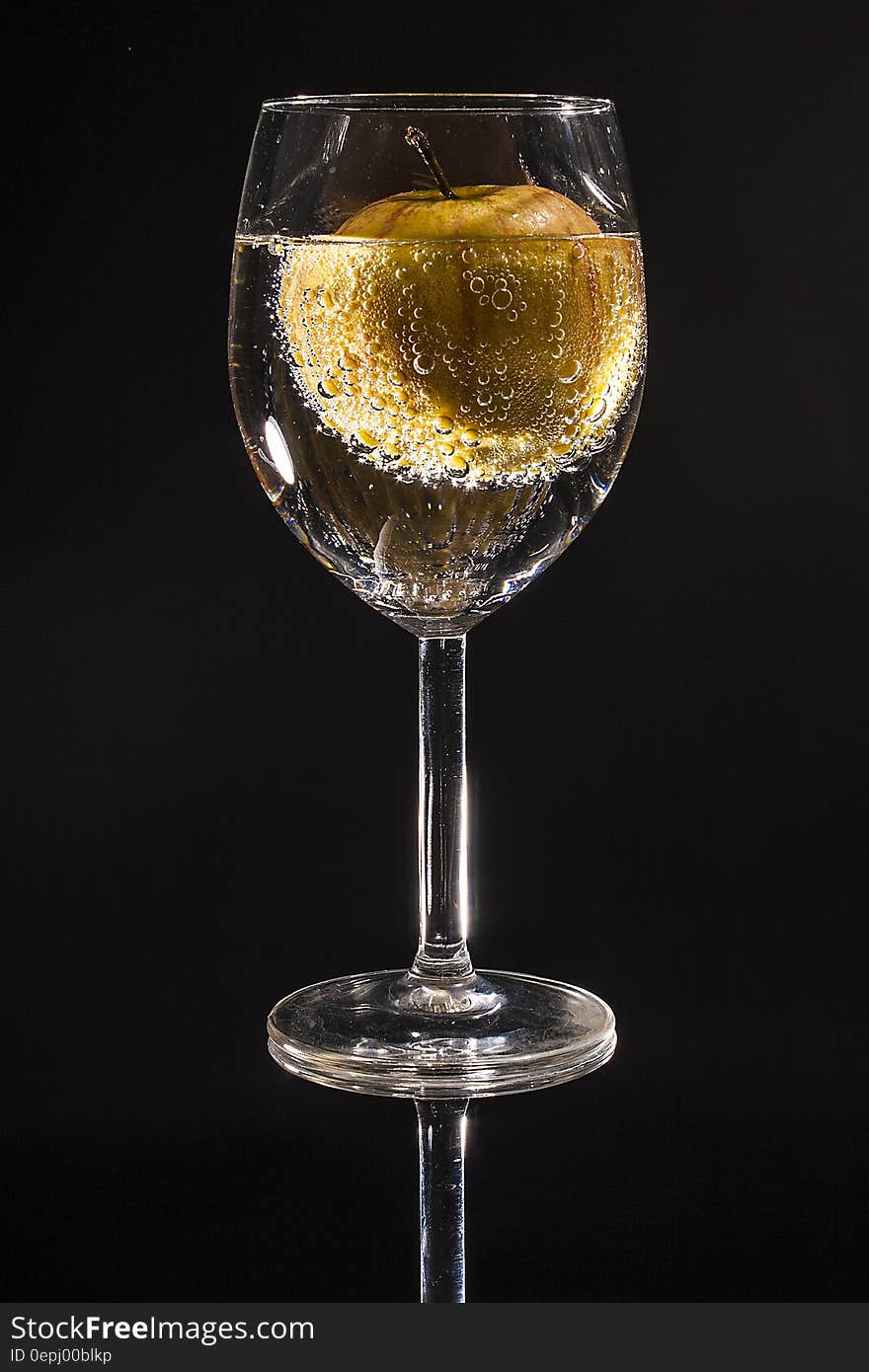 Clear Wine Glass Filled With Clear Beverage With Yellow Round Fruit