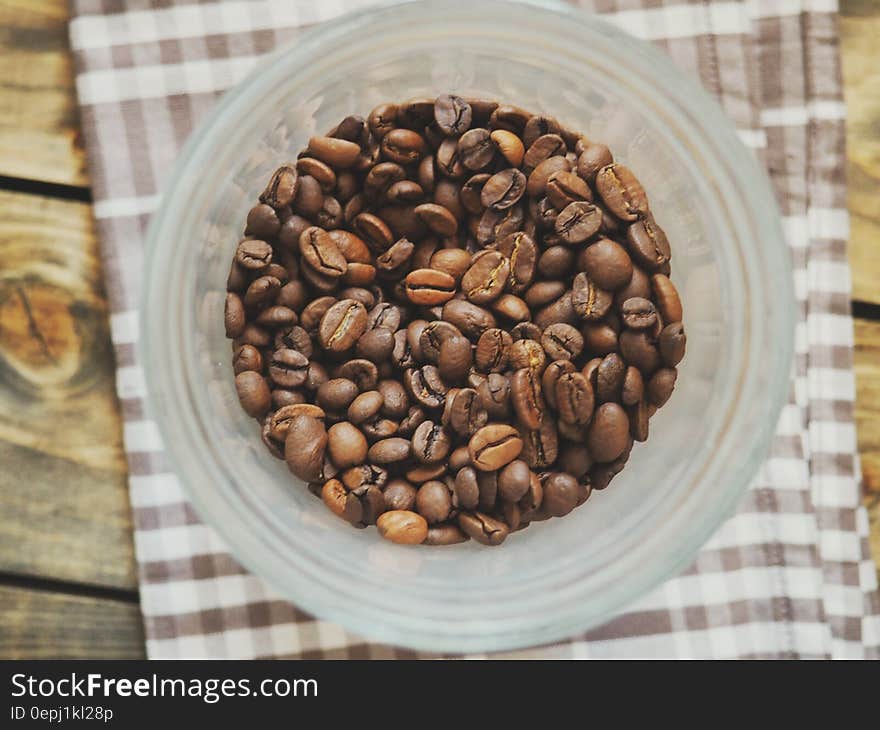 Overhead of glass bowl with roasted coffee beans on brown towel on wooden slats. Overhead of glass bowl with roasted coffee beans on brown towel on wooden slats.