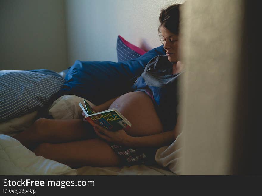 Pregnant Woman Sitting on Bed and Reading Book