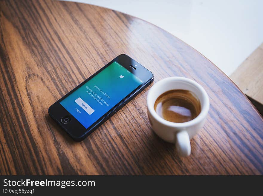 Smartphone and white coffee cup on wooden tabletop. Smartphone and white coffee cup on wooden tabletop.