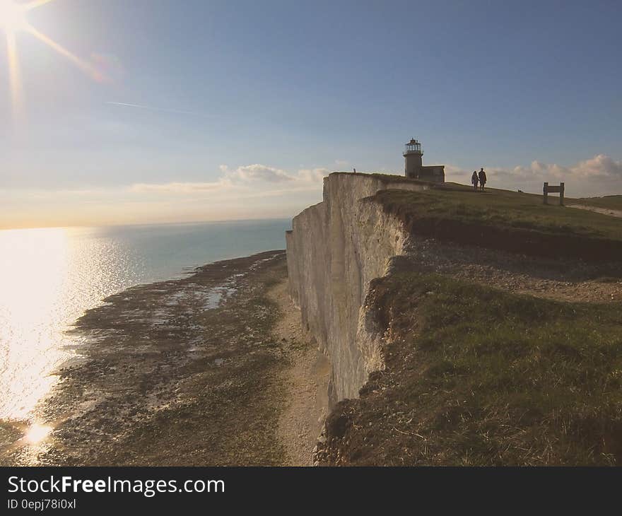 Lighthouse on cliff overlooking sandy beach.