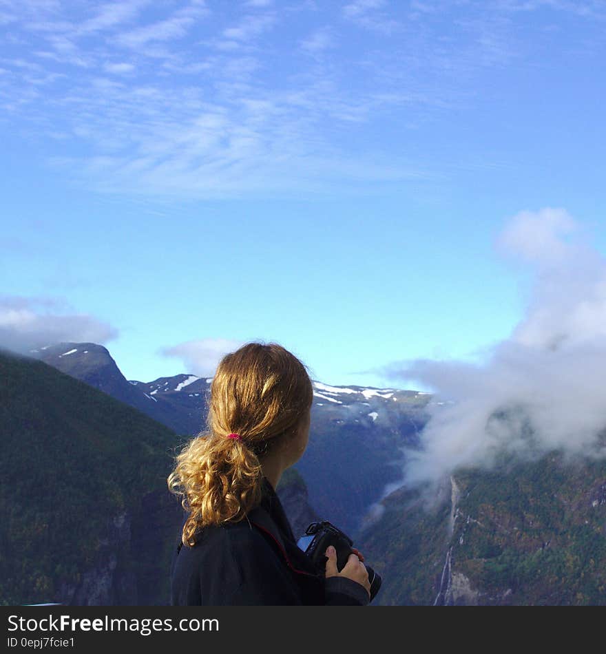 Woman Wearing Black Long Sleeve Shirt Watching on Green and Brown Mountain Under White and Blue Sky during Daytime