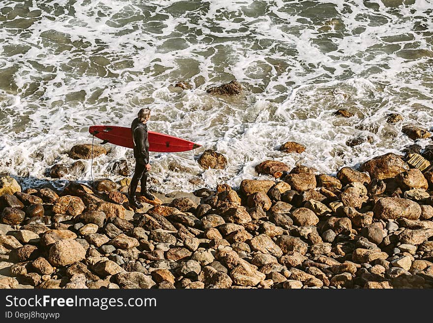 Man Wearing Wetsuit and Holding Red Surfboard on Shore