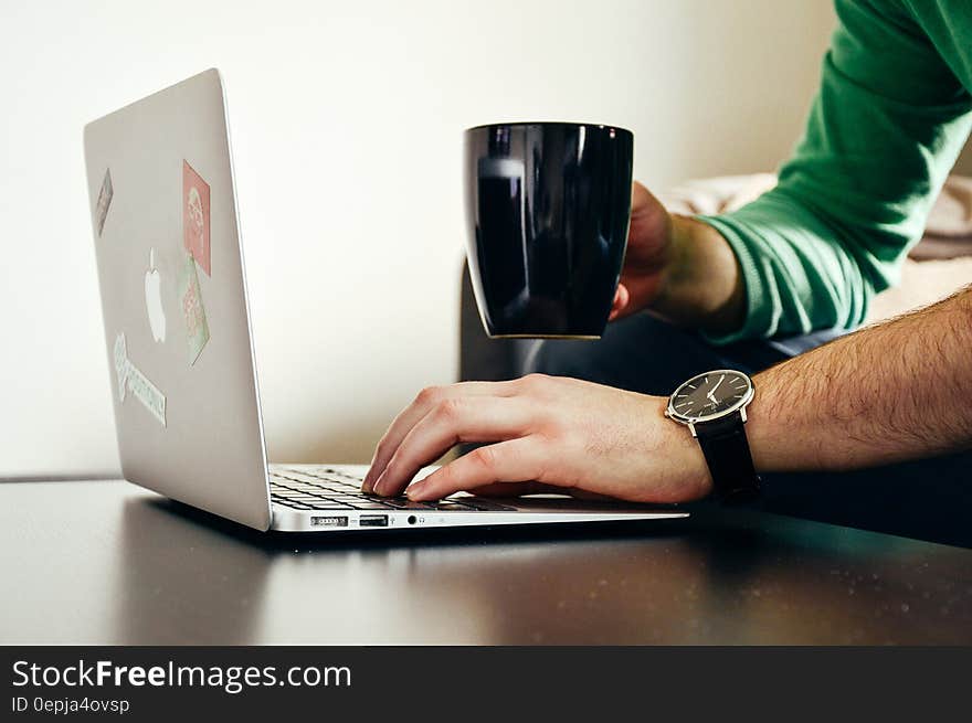 Person Wearing Green Long Sleeve Shirt Holding Black Ceramic Mug and Macbook Air