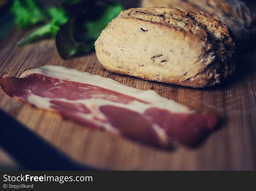 Close up of sliced bacon and bread with lettuce on wooden cutting board.