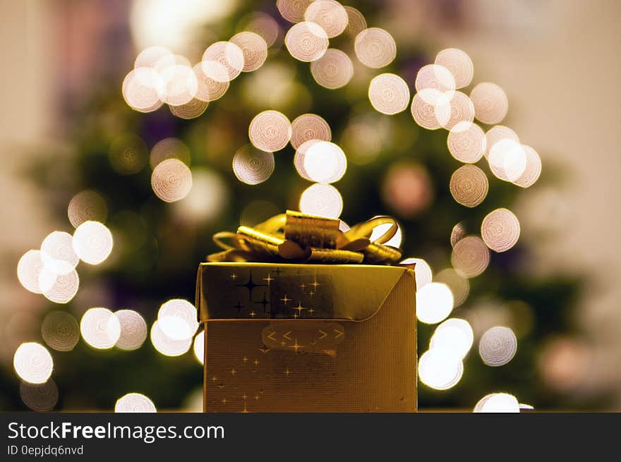 Golden gift in front of bokeh lights on Christmas tree.