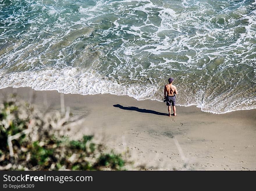 Man in Gray Shorts Standing on White Sand Beach during Daytime