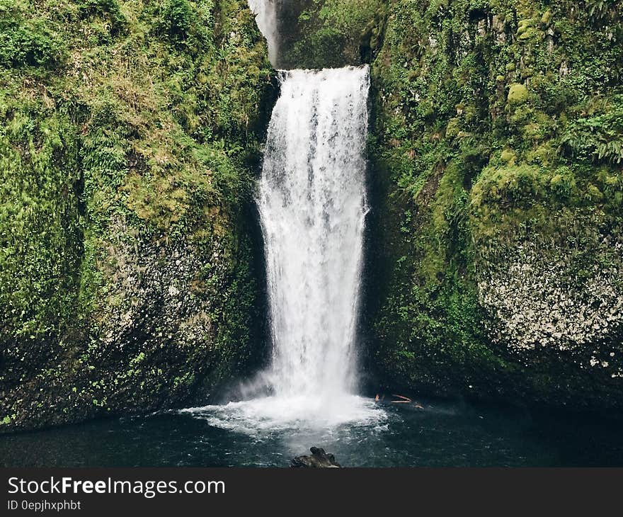 Waterfall over green cliff into countryside pool. Waterfall over green cliff into countryside pool.