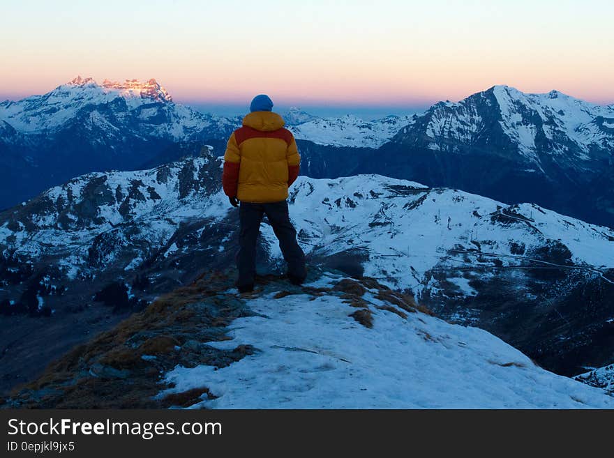 Person in Orange and Red Winter Jacket on Top of Snow Covered Mountain