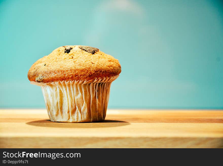 Close up of muffin in paper wrapping on wooden board. Close up of muffin in paper wrapping on wooden board.