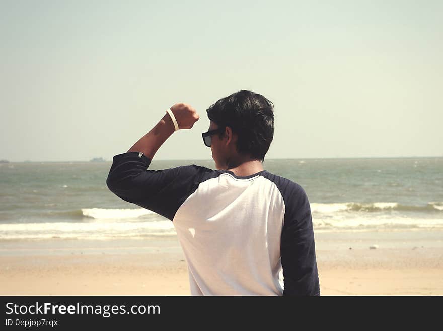 Man in White and Black Raglan Shirt Standing in the Seashore at Daytime