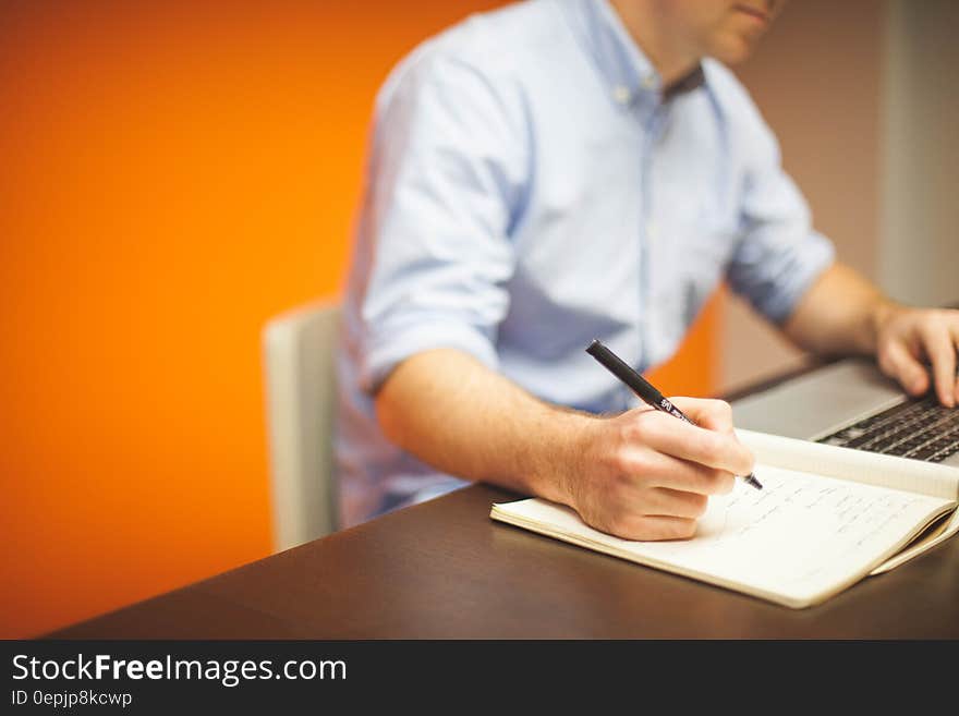 Close up of man writing on tablet while working on computer at desk. Close up of man writing on tablet while working on computer at desk.