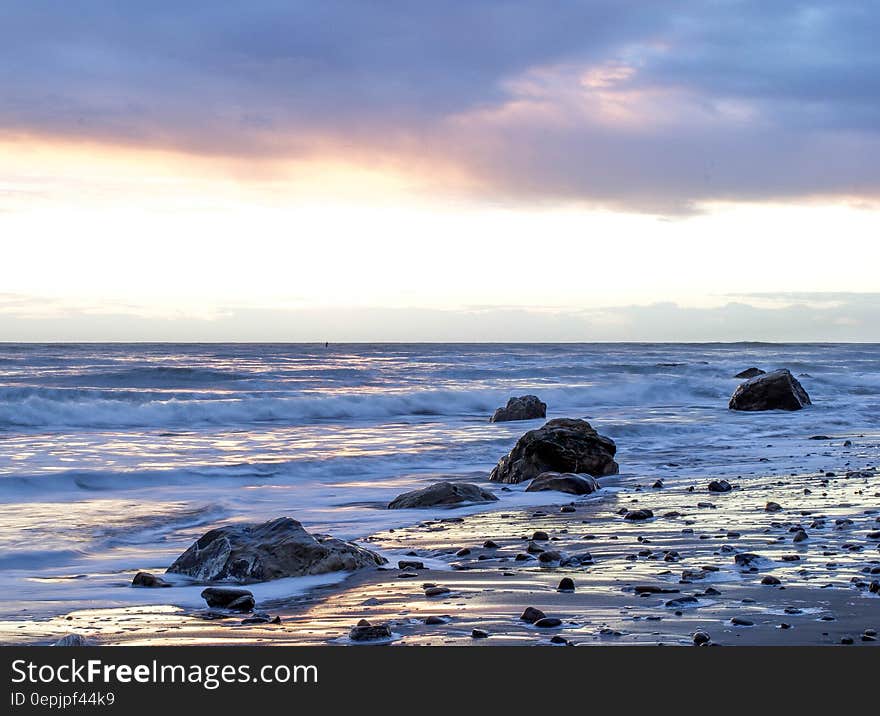 Waves washing over rocky beach with blue and pink clouds in sky. Waves washing over rocky beach with blue and pink clouds in sky.