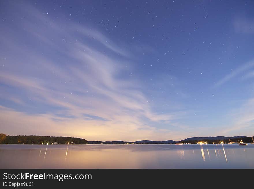 A view of a lake with blue skies and sun setting in the horizon. A view of a lake with blue skies and sun setting in the horizon.