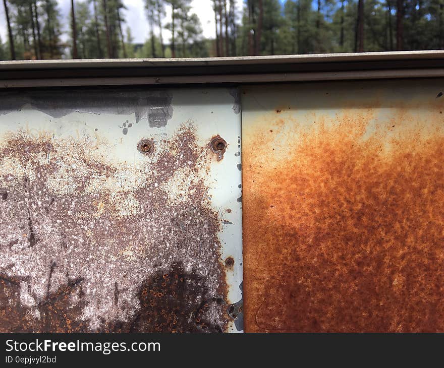 Rusty metal sheets outdoors with trees in background on sunny day.