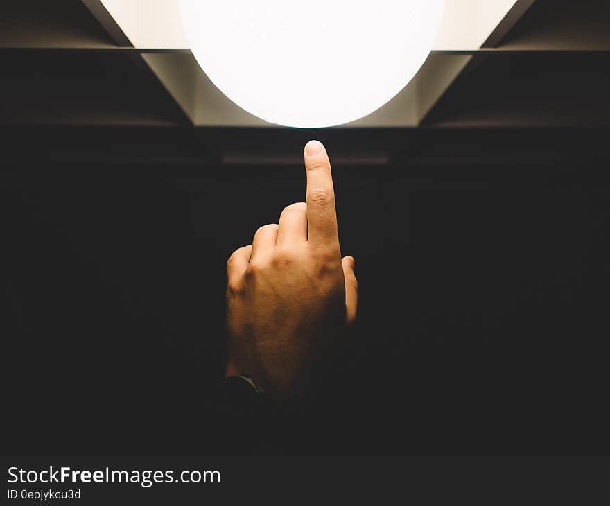 Close up of finger reaching from darkness touching white lamp. Close up of finger reaching from darkness touching white lamp.