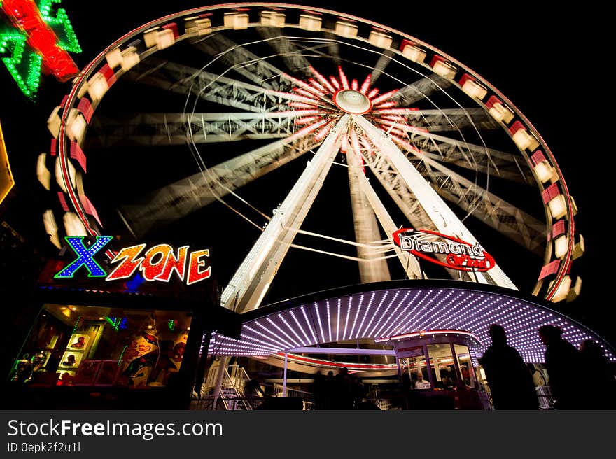 Ferris wheel in funfair at night with motion blur, silhouetted people in foreground.