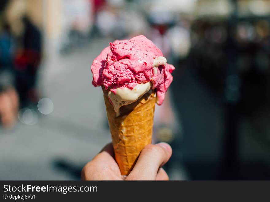 Hand of person holding strawberry ice cream cone outdoors. Hand of person holding strawberry ice cream cone outdoors.