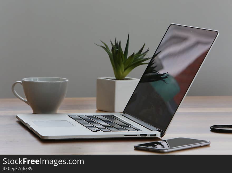 A laptop computer on a desk with a smartphone, houseplant and a coffee cup. A laptop computer on a desk with a smartphone, houseplant and a coffee cup.