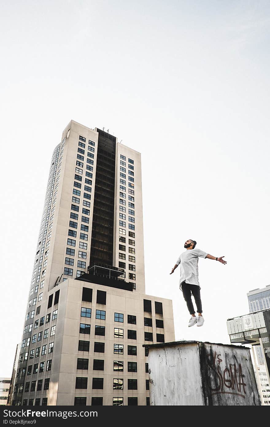 Man Wearing White Long Sleeve Shirt Beside White and Black High Rise Building