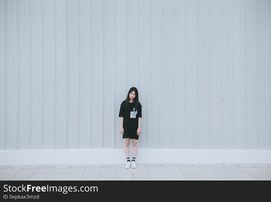 Woman in Black Elbow Sleeve Shirt and Black Shorts Standing Behind White Wall