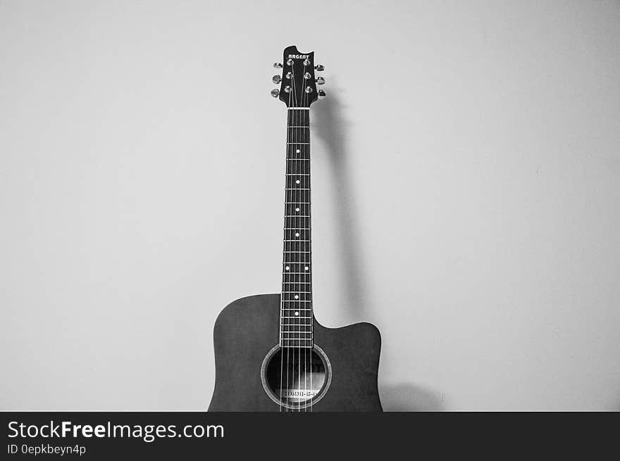 Close up of acoustic guitar against wall in black and white.