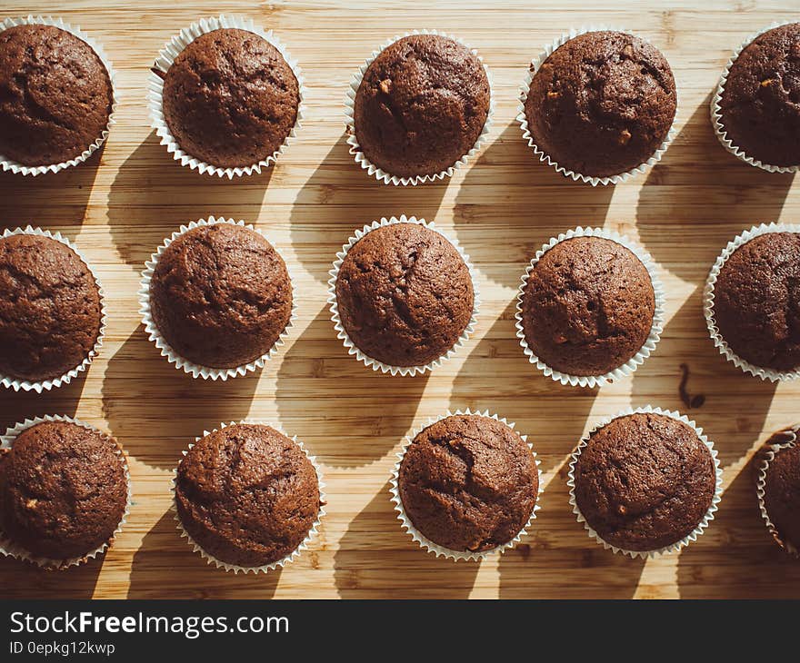 Overhead of baked muffins in paper wrappers on wooden board. Overhead of baked muffins in paper wrappers on wooden board.