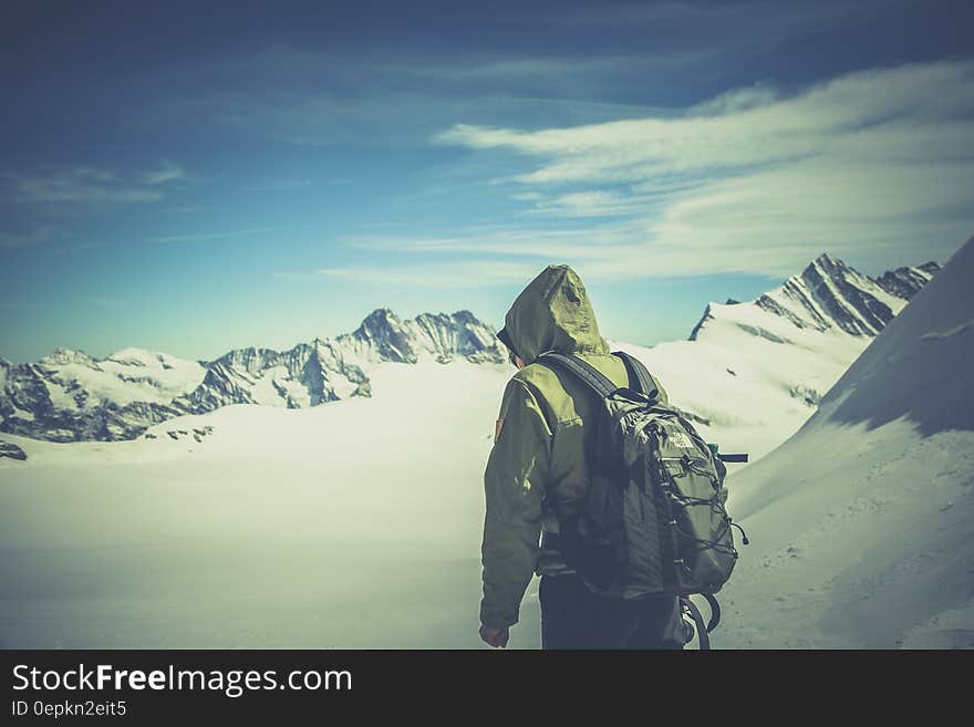 Person Wearing Green Jacket Walking on White Snow Covered Mountain