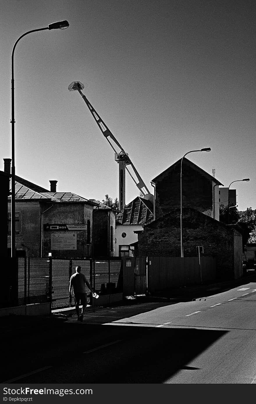 Man walking along fence line of industrial lot in urban black and white scene. Man walking along fence line of industrial lot in urban black and white scene.