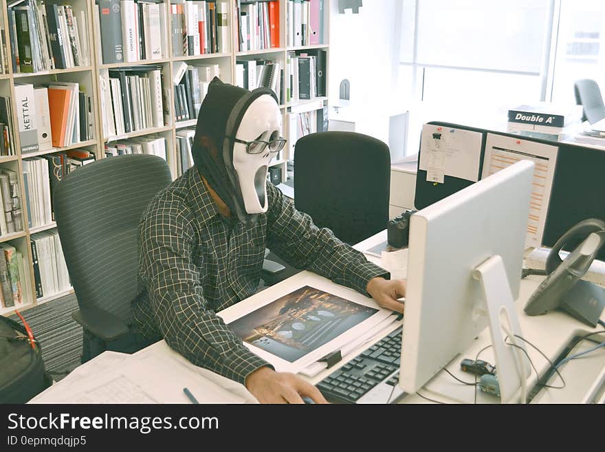 Person Wearing Scream Mask and Black Dress Shirt While Facing Computer Table during Daytime