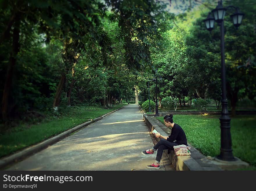 Man in Black Sweater Reading Book While Seated on Concrete