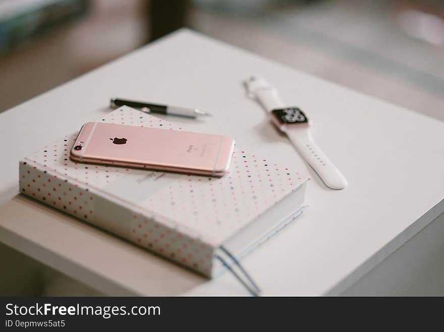 Rose Gold Iphone 6 S on Top of White Covered Book