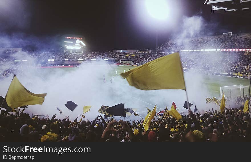 Big crowds attending a football match waving yellow flags but play not visible due to smoke from fireworks set off by hooligans. Big crowds attending a football match waving yellow flags but play not visible due to smoke from fireworks set off by hooligans.